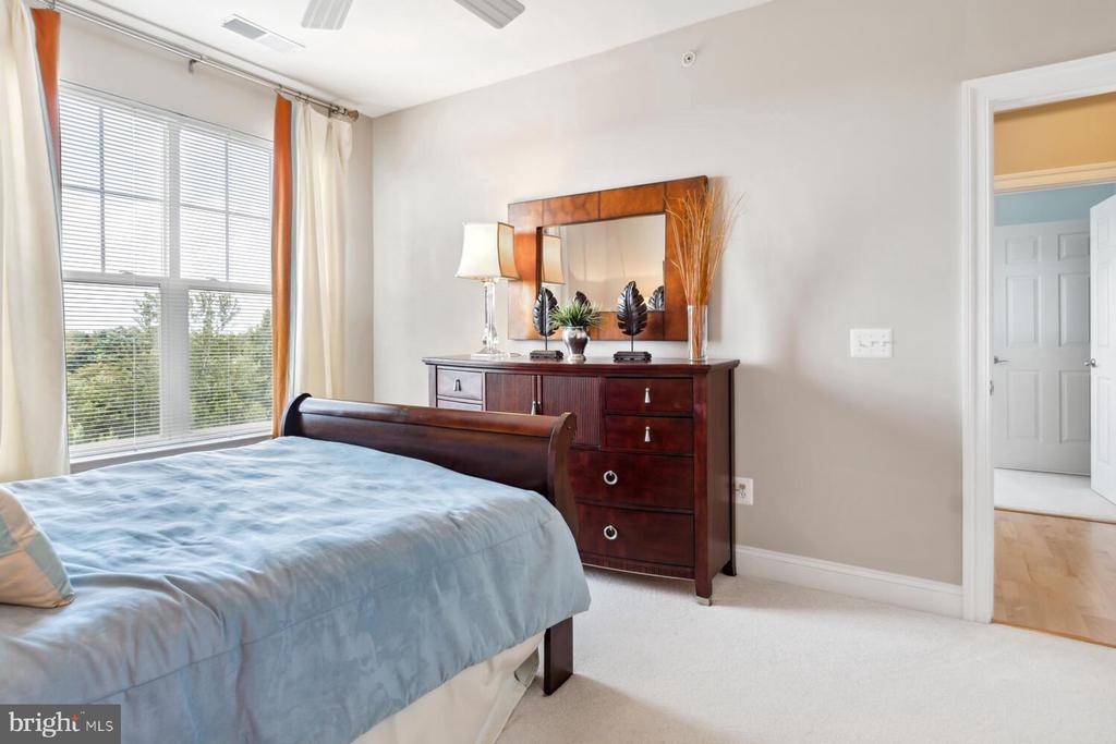 Furnished bedroom with pale blue bedding, dark wood furniture, and a large window with white blinds.