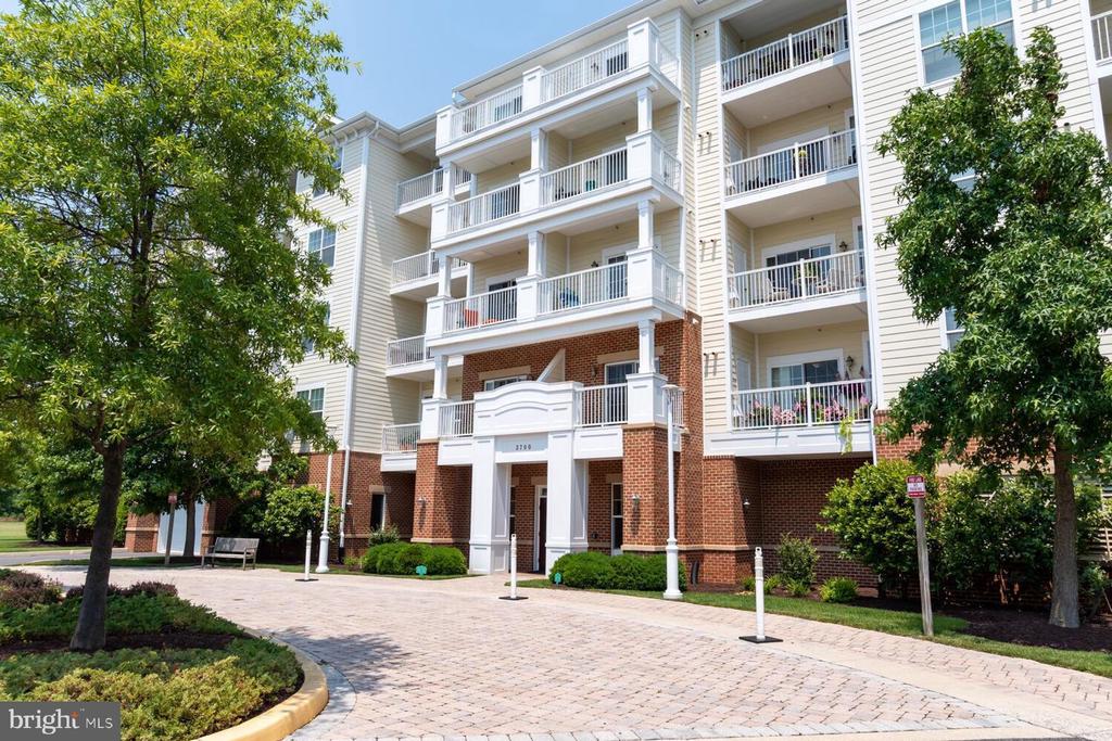 Multi-story apartment building with white balconies, a brick entrance, and a brick-paved driveway.