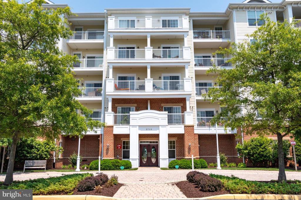 Condominium building with stacked white balconies, a brick entrance, and landscaped grounds.
