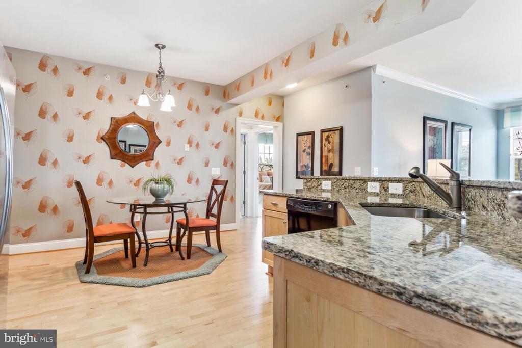 Dining nook beside a granite kitchen counter, with patterned wallpaper and a round glass-top table.