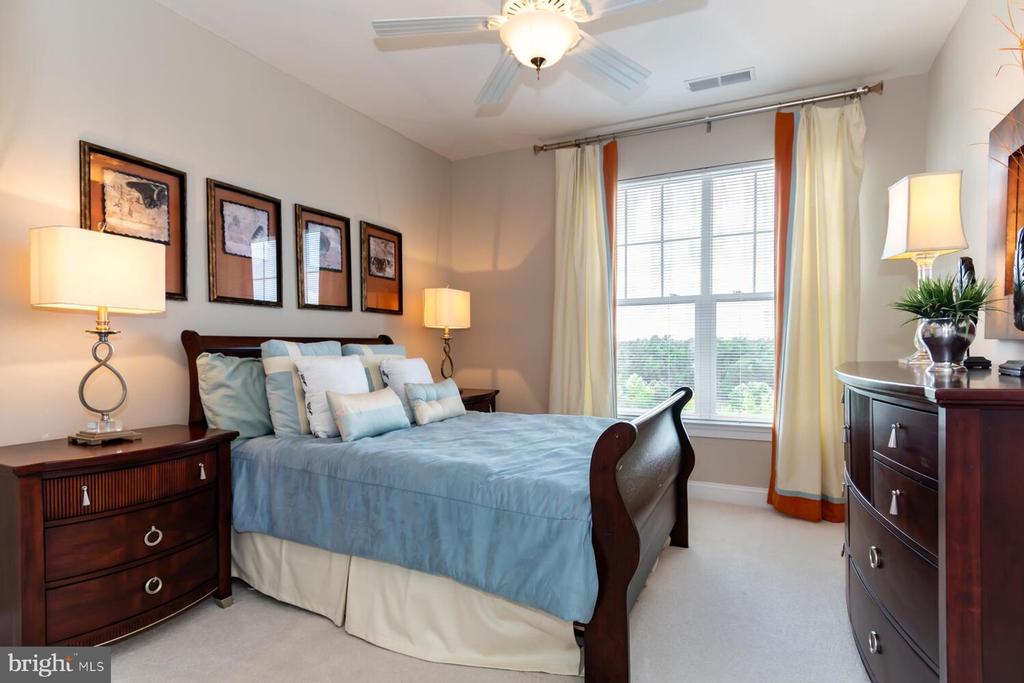 Bedroom with pale blue bedding, dark wood furniture, framed artwork, and a large curtained window.