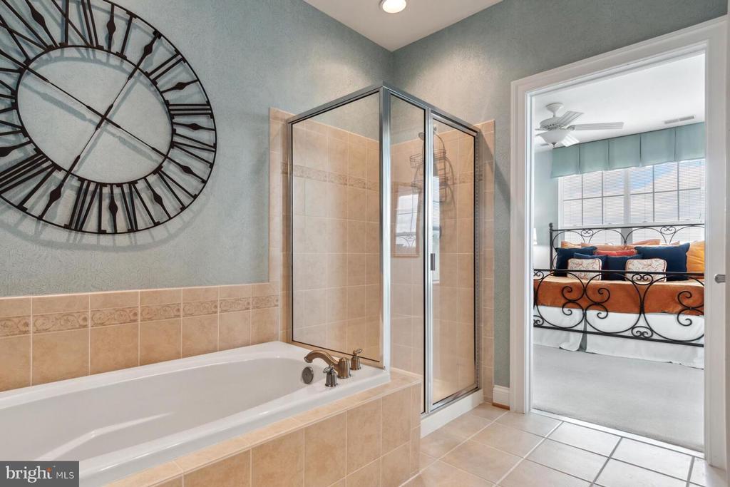 Bathroom with a tiled soaking tub and glass shower, opening to a bright bedroom.