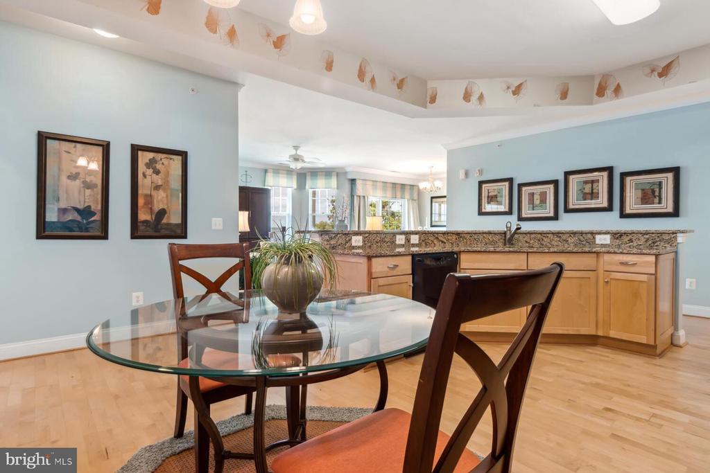 Dining area with a glass-top table and dark wood chairs beside an open kitchen.