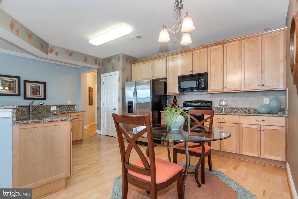 Kitchen and dining area with light wood cabinets, granite counters, and a round glass table.