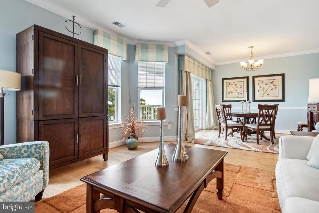 Furnished living and dining area with large windows, dark wood furniture, and a chandelier.