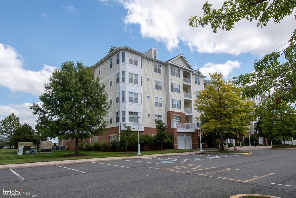 Multi-story condominium building with balconies, a brick ground floor, and parking spaces.