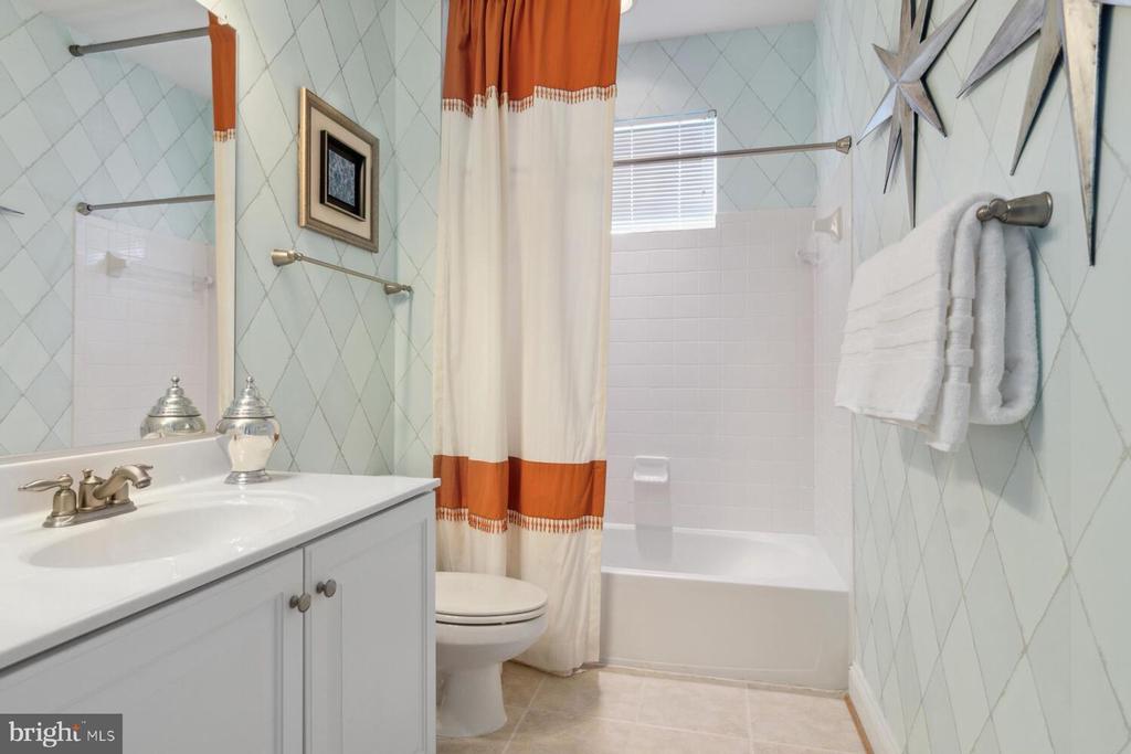 Bathroom with pale diamond-patterned tile, a white vanity, and a tub behind a rust-and-white curtain.