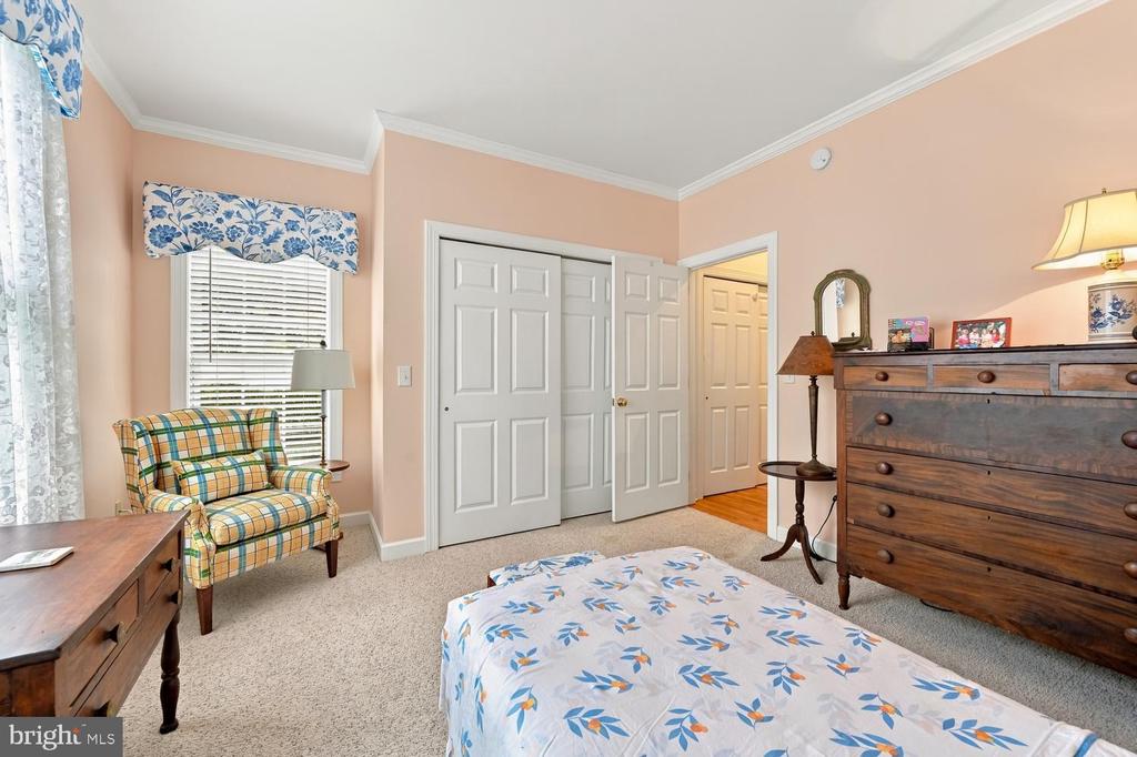 Bedroom with floral bedding, a plaid armchair, and open white closet doors.