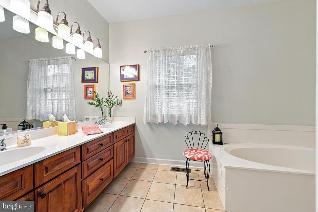 Bathroom with a long wood double vanity, lace-curtained windows, and a built-in soaking tub.