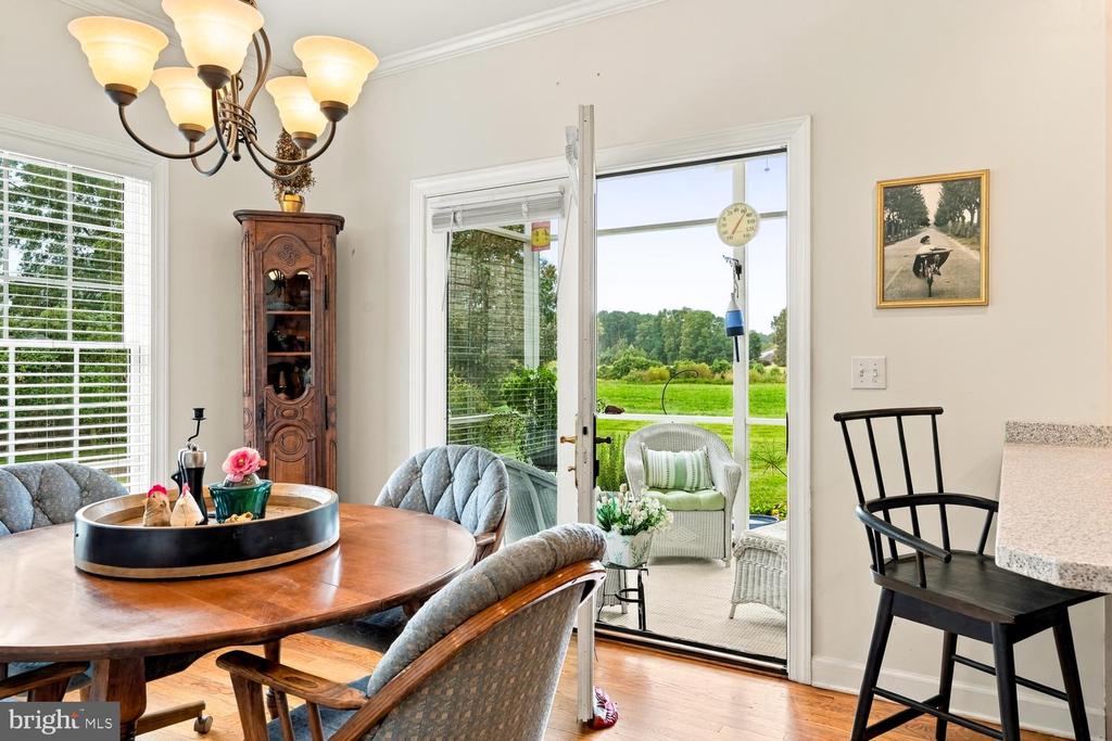 Dining room with a round wooden table and open doors to a screened porch and lawn.