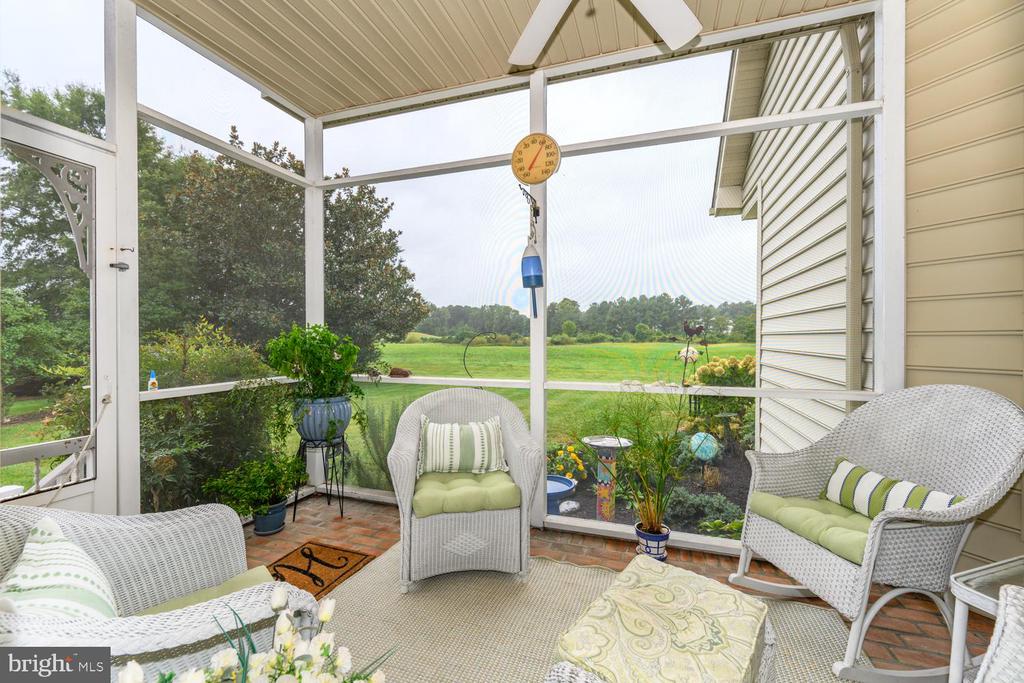 Screened porch with white wicker seating and potted plants overlooking a broad green lawn.