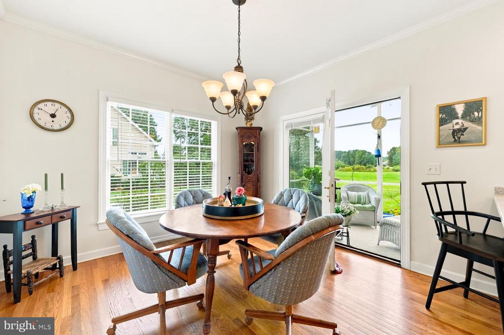 Dining room with a round wooden table, chandelier, hardwood floors, and glass doors opening to a green lawn.