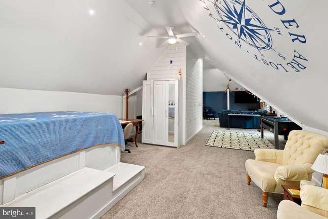 Attic recreation room with a blue-covered raised bed, game area, and cream lounge chairs.