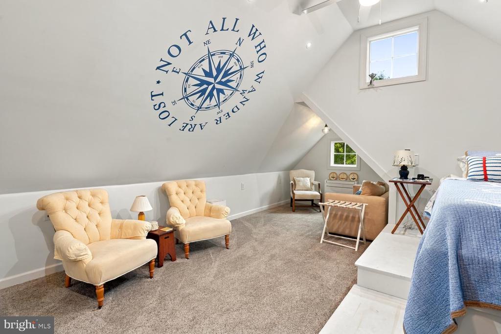 Furnished upper-level bedroom with a sloped ceiling, compass wall graphic, and upholstered chairs.