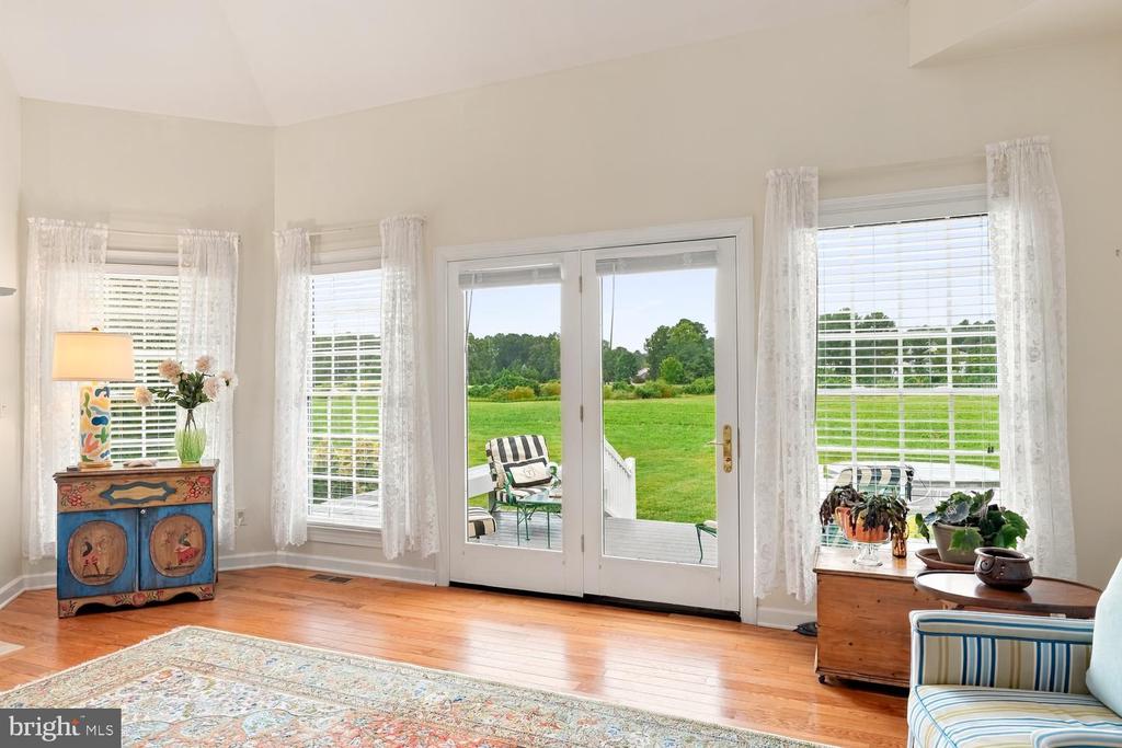 Furnished sitting area with French doors opening onto a deck and expansive green lawn.