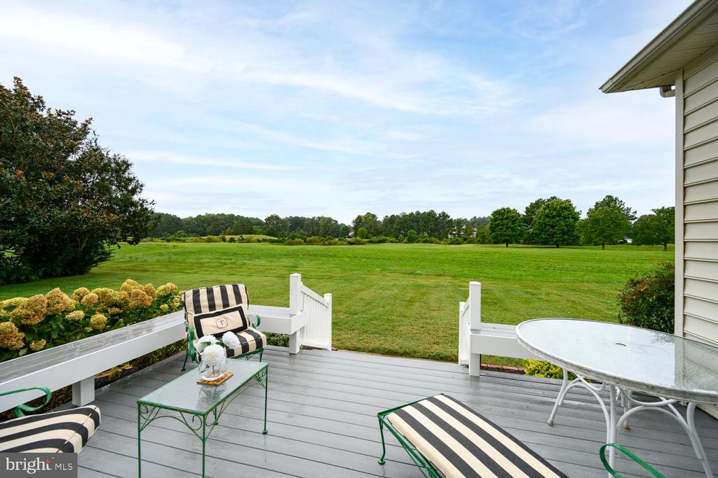 Deck with striped lounge chairs and patio table overlooking a broad green lawn.