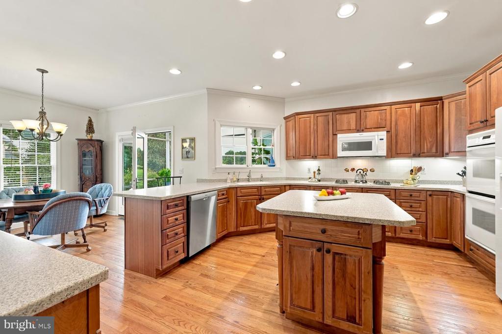 Kitchen with a granite-topped island, warm wood cabinetry, stainless appliances, and hardwood floors.