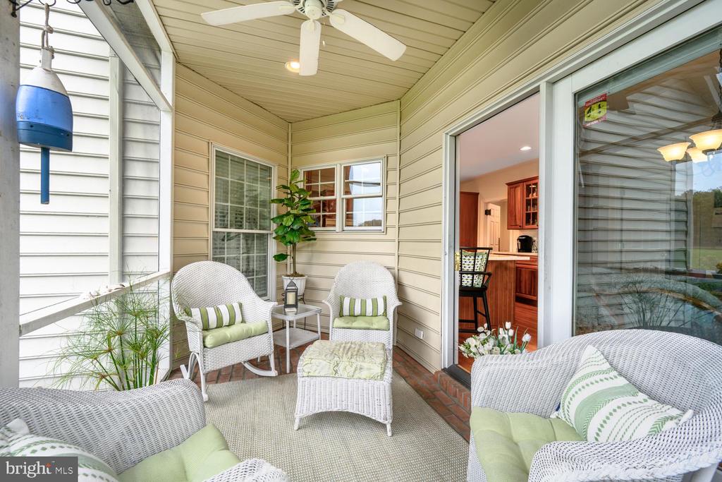 Covered porch with wicker seating, green cushions, and a ceiling fan beside a sliding glass door.