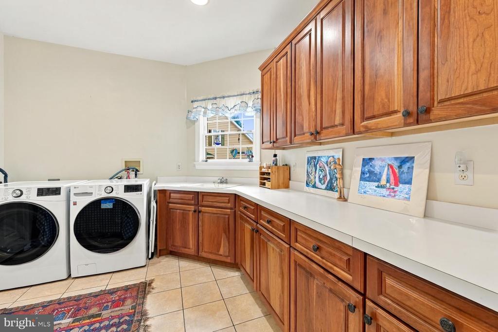 Laundry room with front-loading washer and dryer, wood cabinetry, and a long white countertop.
