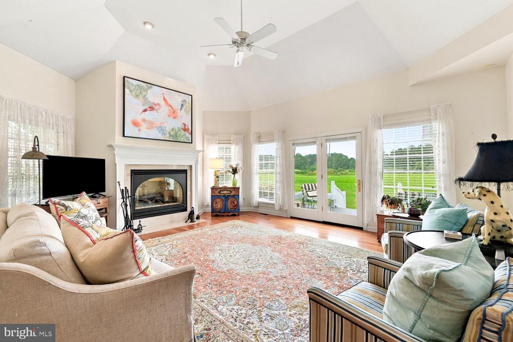 Living room with a white fireplace, patterned rug, and French doors overlooking a green lawn.