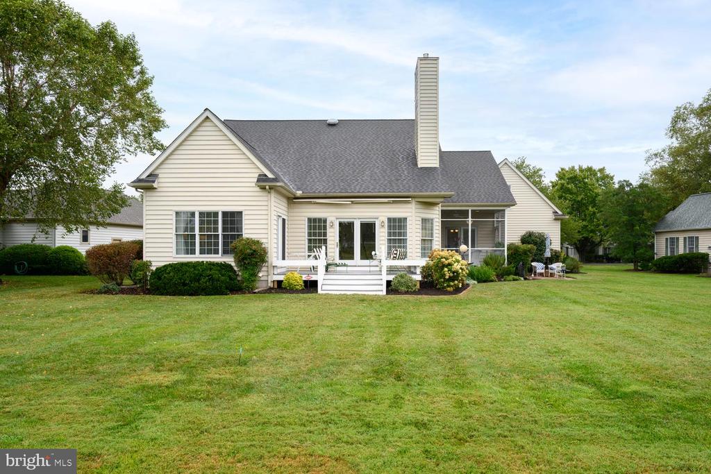 Rear of a light-colored house with a raised deck, covered patio, and broad lawn.