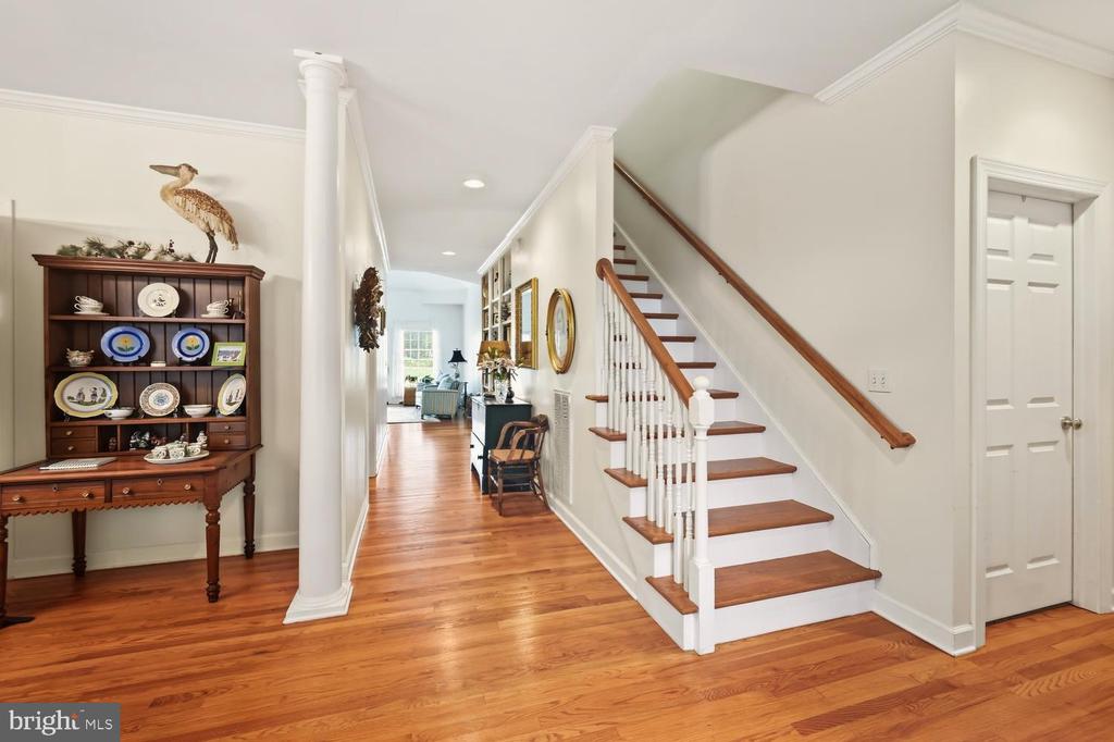Entry hall with a wood-tread staircase, hardwood floors, and a china cabinet beside a white column.