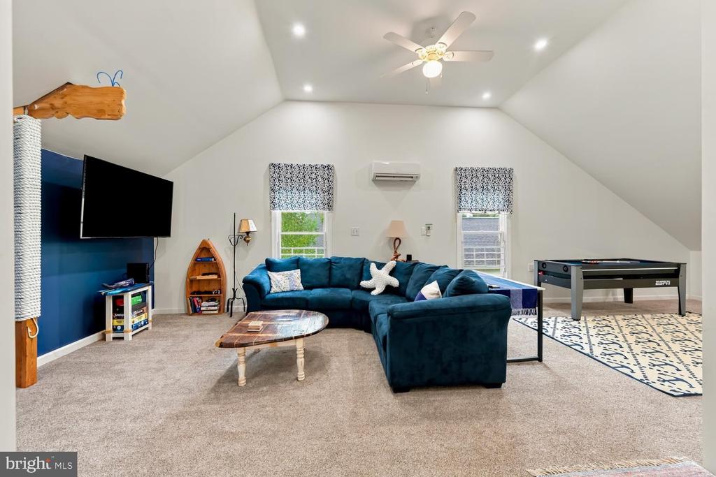 Upstairs living room with vaulted ceiling, teal sectional, wall-mounted TV, and foosball table.