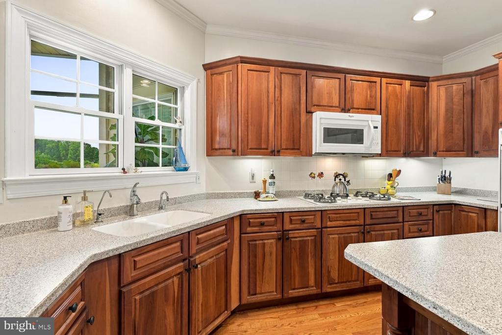 Kitchen with reddish wood cabinets, speckled countertops, and a sink beneath two windows.
