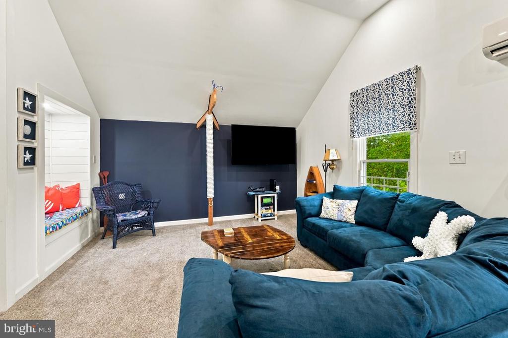 Living room with a teal sectional, vaulted ceiling, navy accent wall, and built-in window seat.