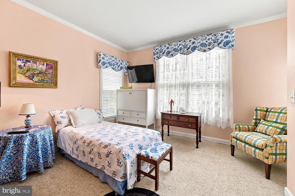 Furnished bedroom with a floral bedspread, peach walls, and a plaid armchair.