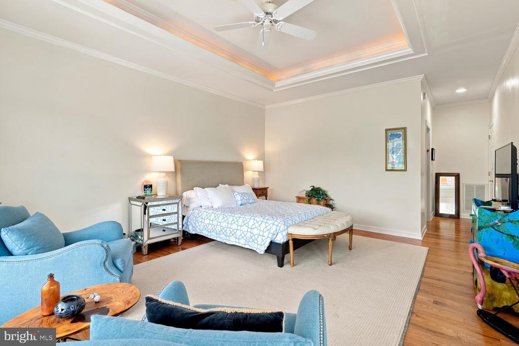 Furnished bedroom with a tray ceiling, ceiling fan, and blue sitting area.