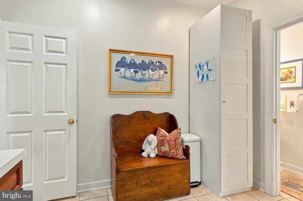 Tiled interior with a wooden storage bench, tall white cabinet, and framed waterfowl artwork.