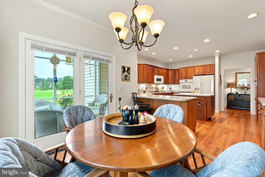 Dining area with a round wooden table, opening into a warm wood kitchen and overlooking a green lawn.