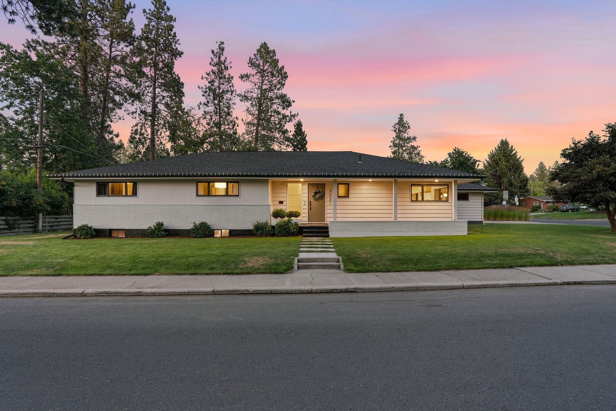 Single-story home with a broad dark roof, lit windows, and front lawn at dusk.