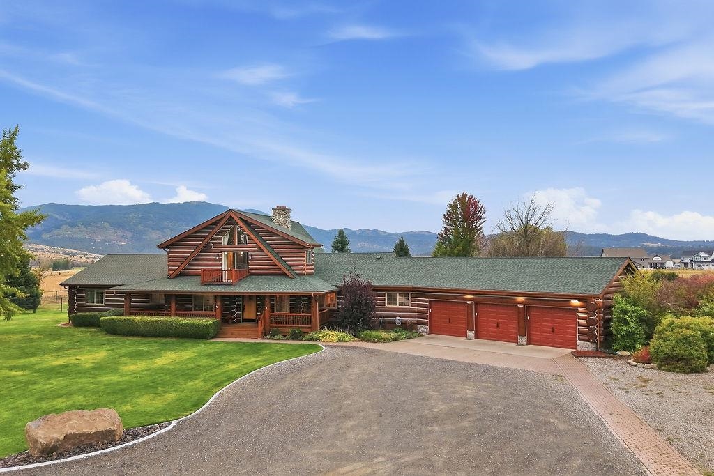 Log home with a timber gable and three-car garage, set against a mountain backdrop.