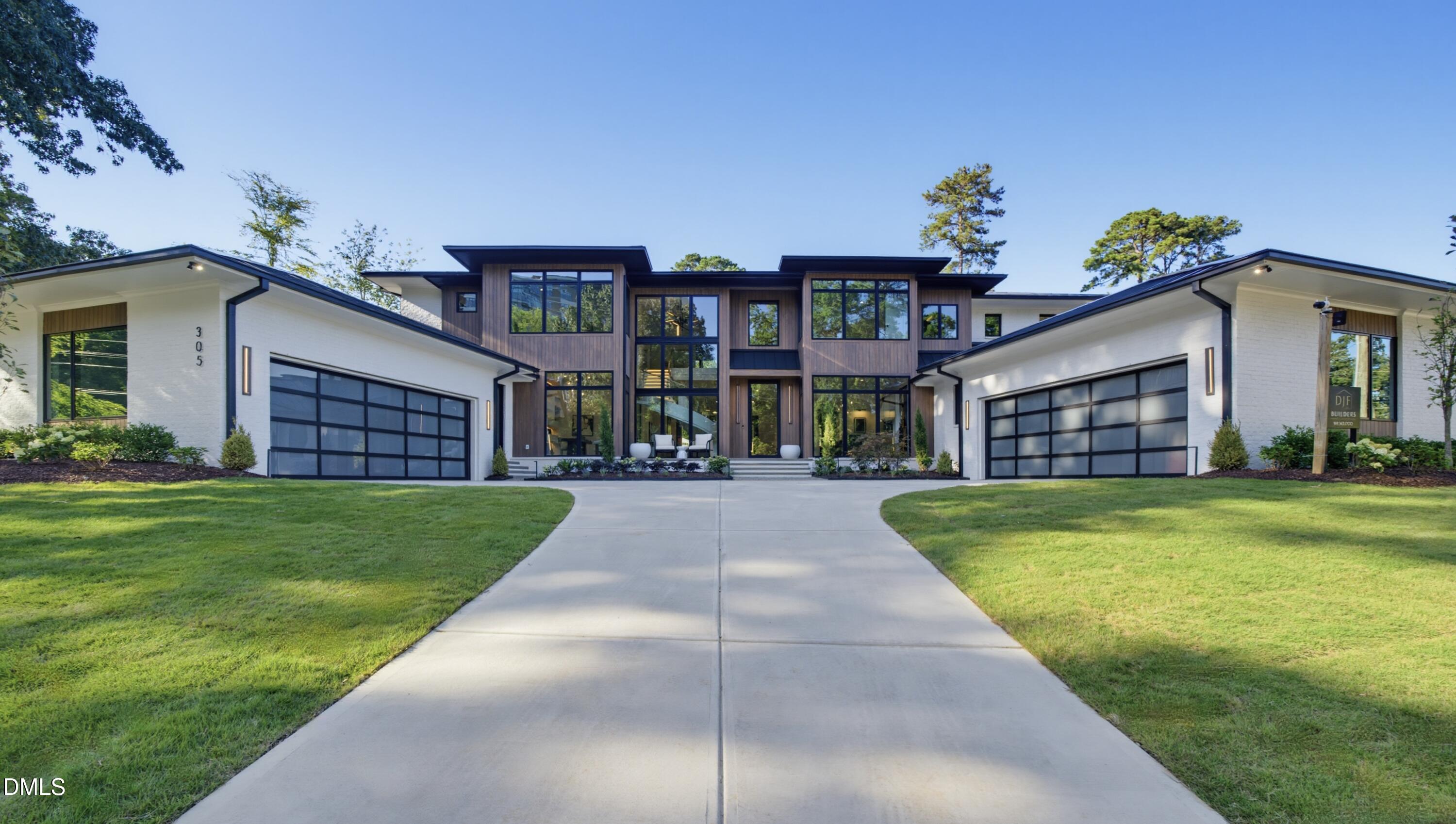 Modern two-story home with dark wood siding, twin glass-paneled garages, and a broad concrete driveway.