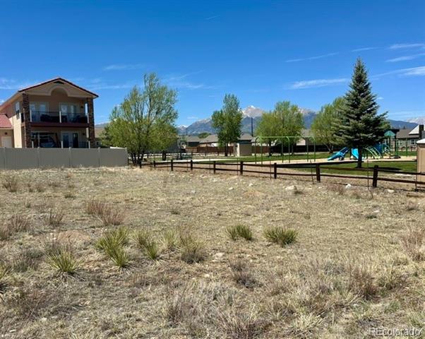 Vacant lot with dry native grasses, neighborhood homes, a playground, and distant mountains.