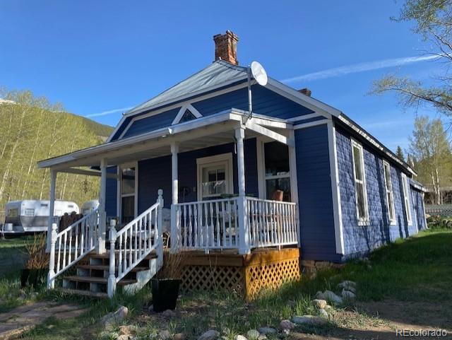 Blue house with a covered porch, white railings, and a brick chimney.