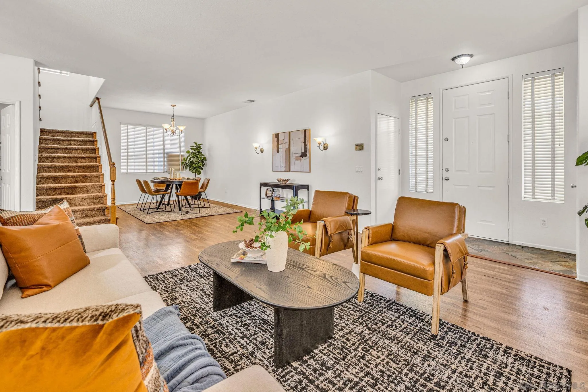Staged living room with caramel leather chairs, patterned rug, staircase, and adjoining dining area.