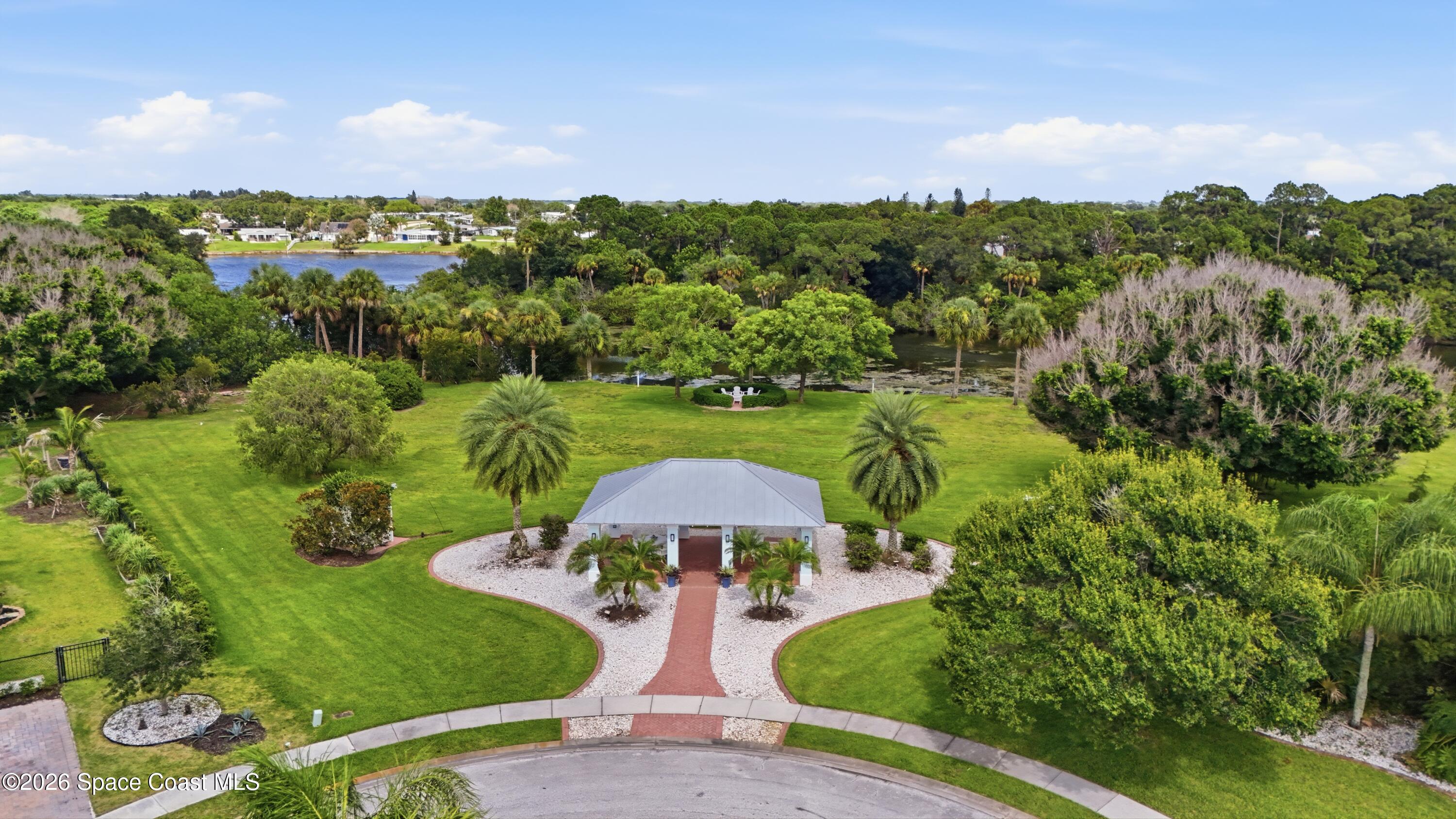 Aerial view of a house amid landscaped grounds, palms, and a pond.