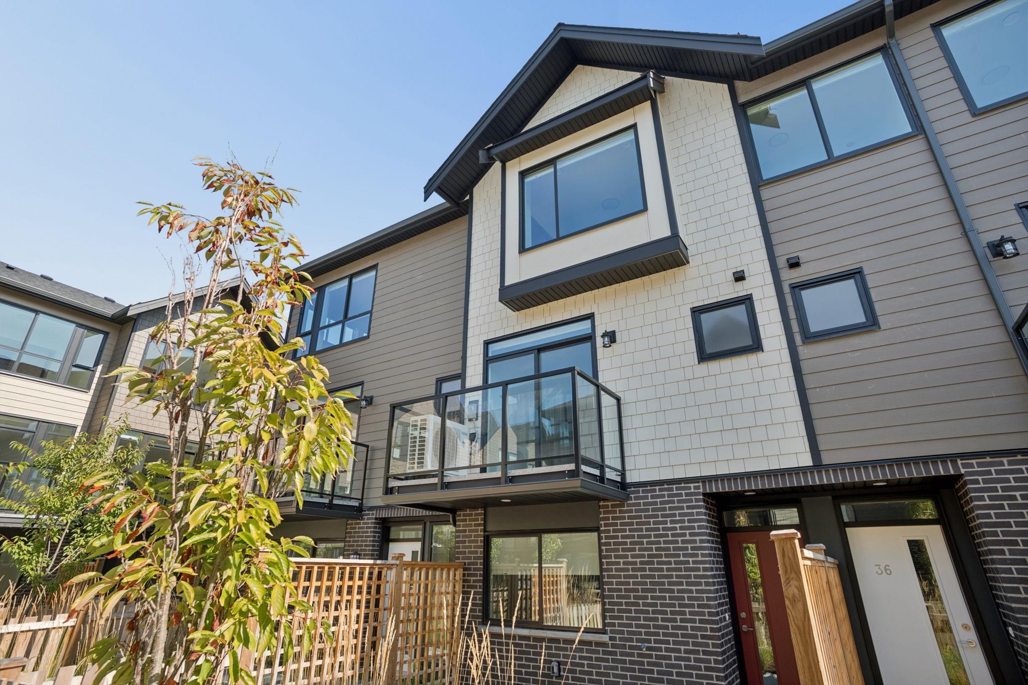 Modern townhouse exterior with glass balconies, contrasting siding and brick, and a leafy tree in front.