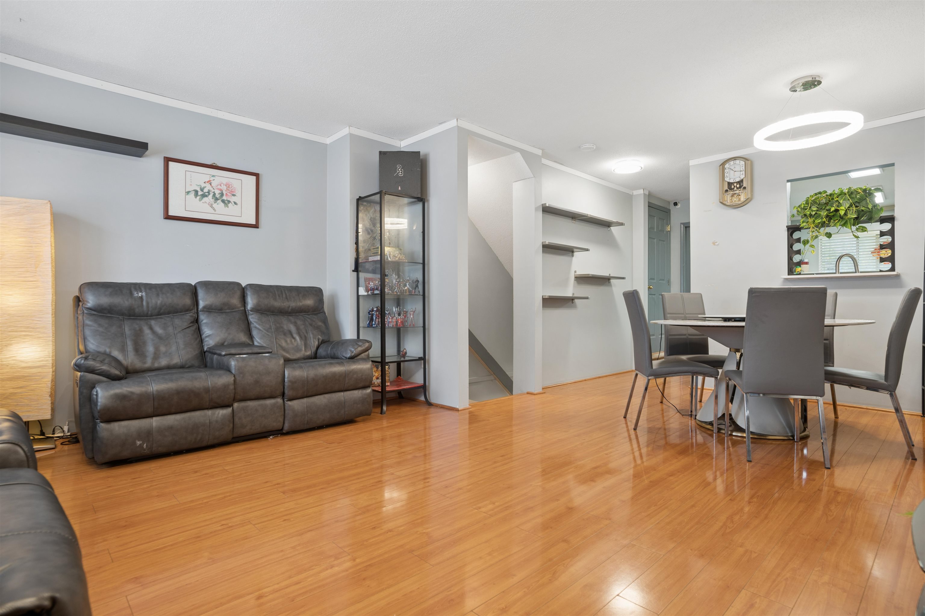 Townhouse living and dining area with wood floors, leather sectional, gray dining set, and central staircase.