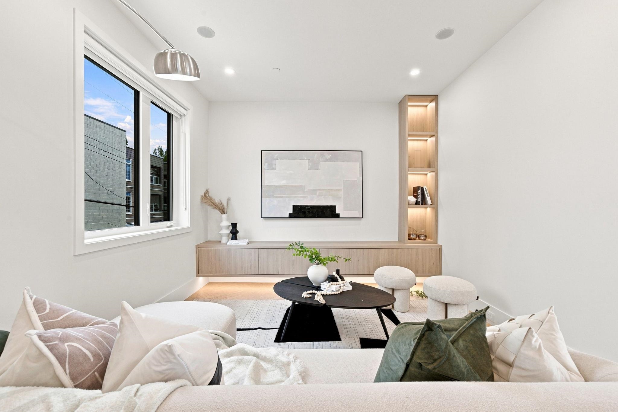 Modern living room with a large window, built-in wood shelving, and a white sofa.