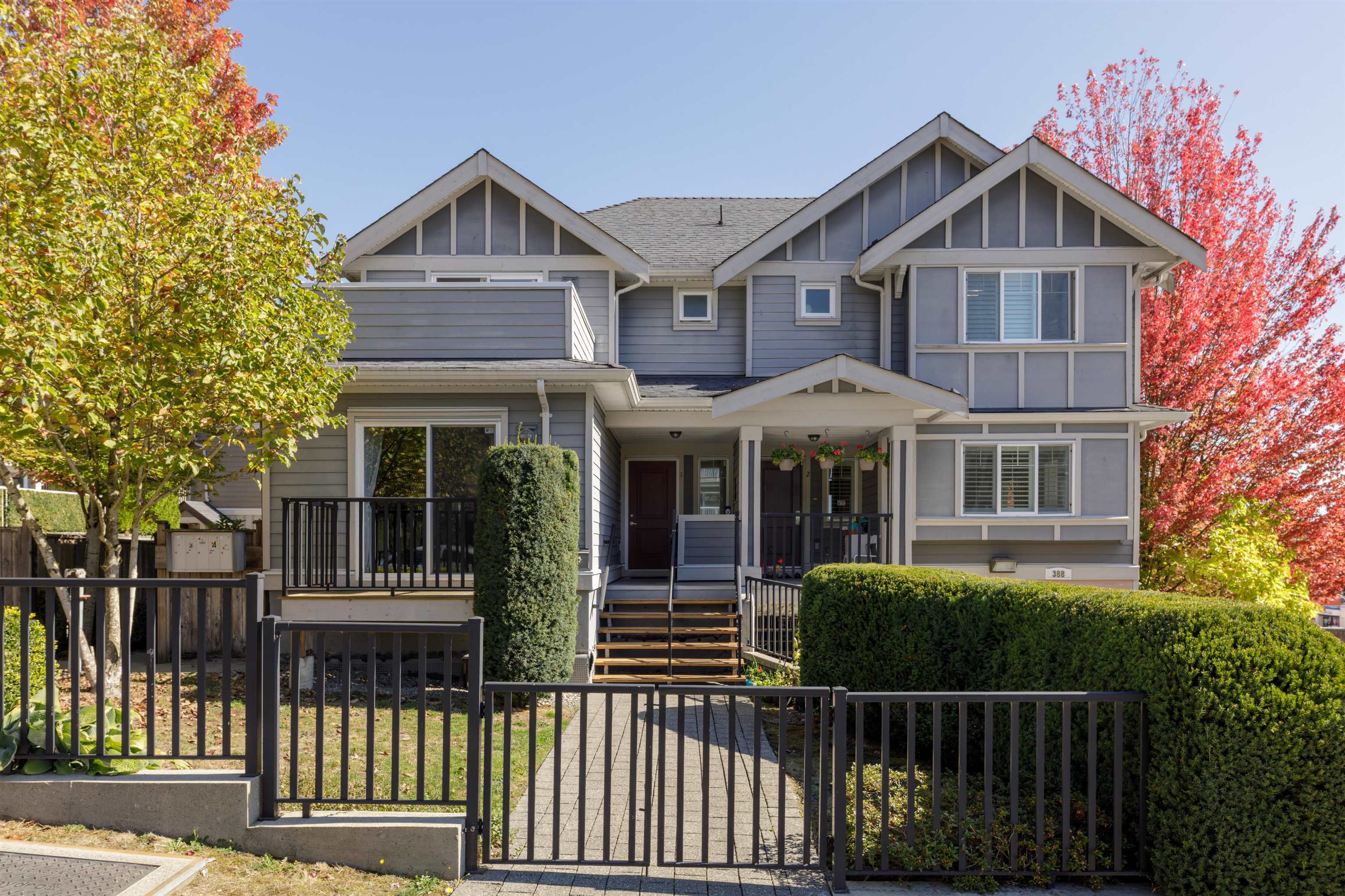 Gray two-story house with gabled roofs, a covered porch, gated walkway, and autumn trees.