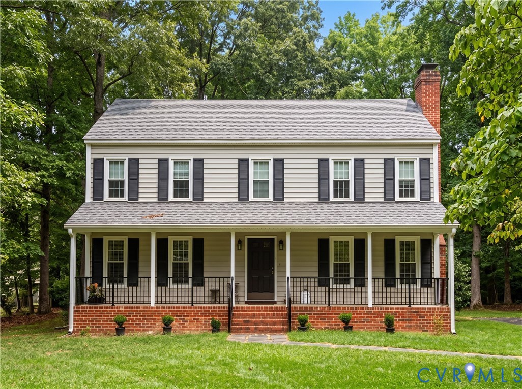 Two-story house with a covered brick-front porch, black shutters, and mature trees.