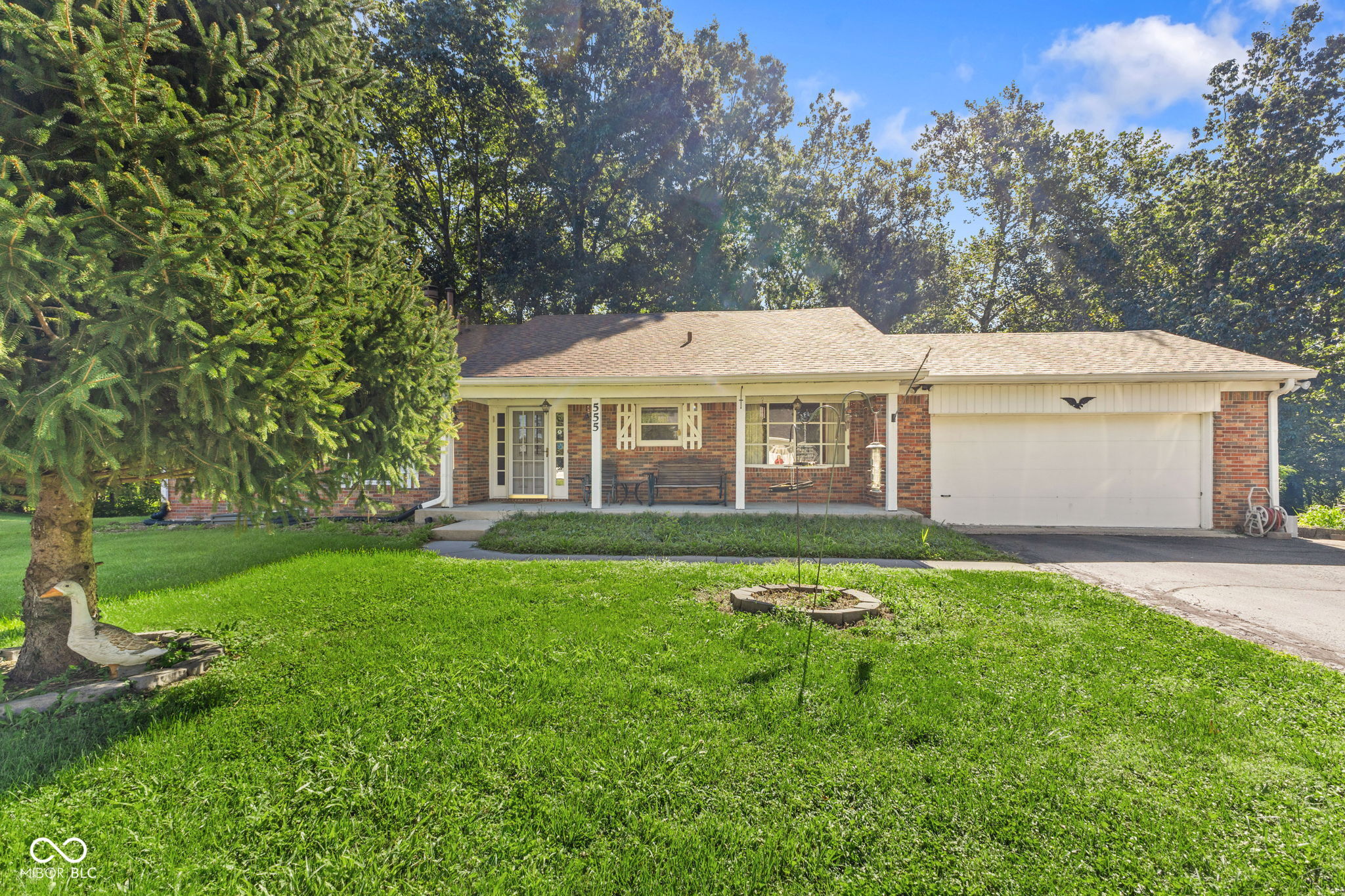 Brick ranch home with attached garage, broad lawn, mature trees, and house number 555.