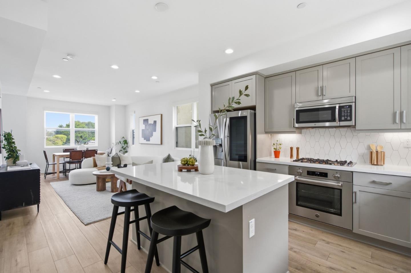 Open-plan kitchen with a large white island, gray cabinets, and adjoining living and dining areas.