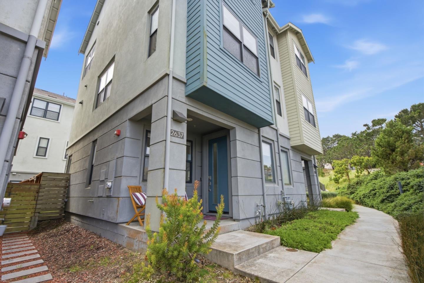 Multi-story home with a blue front door, colorful upper siding, and a landscaped walkway.