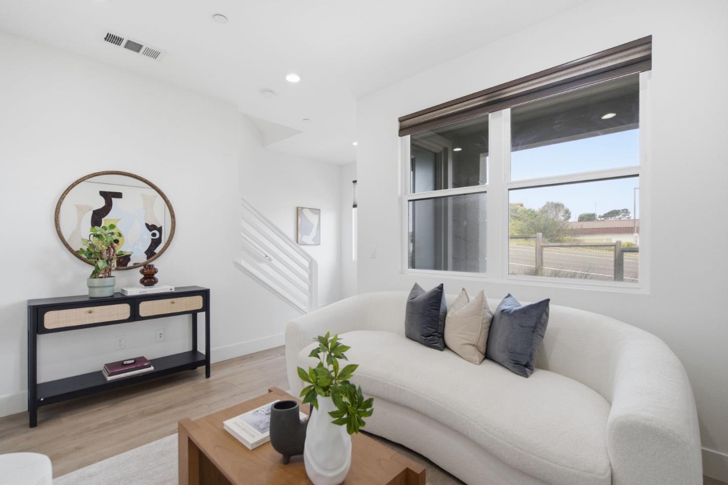 Bright living room with a curved white sofa, large windows, and staircase.