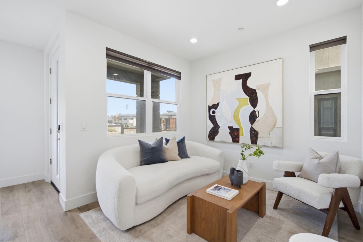 Living room with white sofas, a wood coffee table, and large windows beneath abstract artwork.